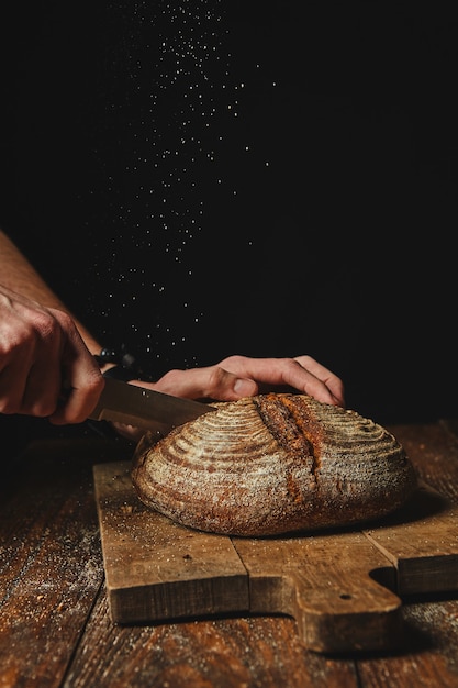 Fresh organic bread on a wooden board cut a man's hands