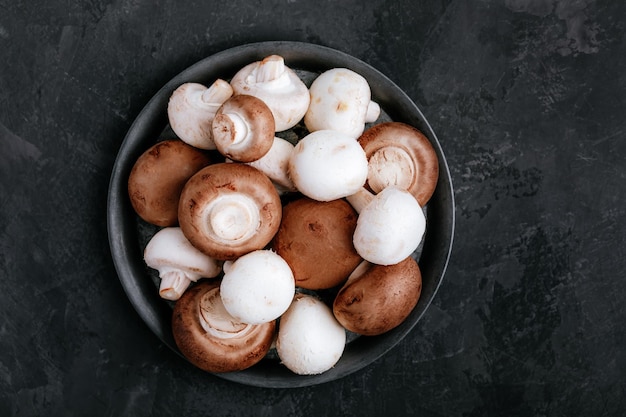 Fresh organic brown and white champignon mushrooms in bowl on dark stone background Top view copy space