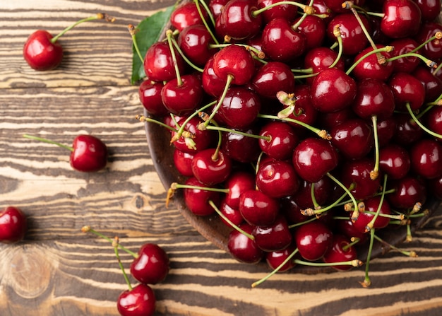 Fresh organic cherries on wooden background in high resolution Fresh sweet red cherries in a wooden bowl and green leaves on a dark brown wooden table