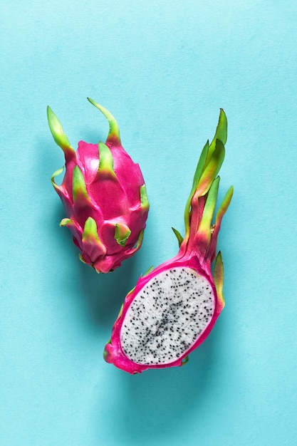 Fresh organic dragonfruit (pitaya or pitahaya) cut in half on blue mint background with shadows. Creative flat layout with trendy exotic fruit in vibrant bold pink and green colors.