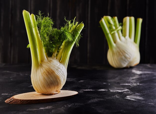 Fresh organic fennel bulbs on wooden stands on a black surface