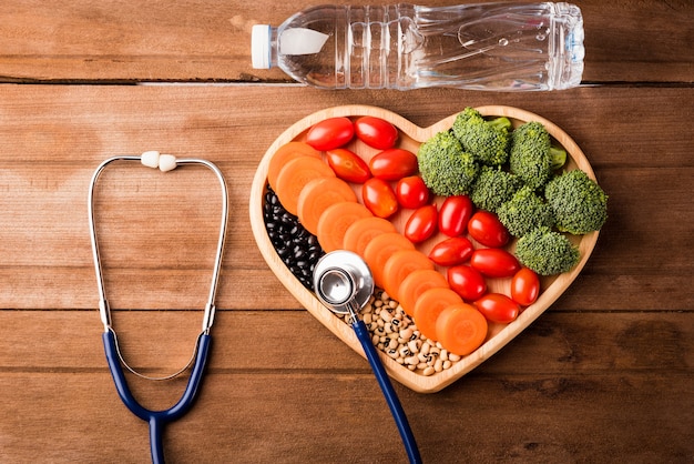 fresh organic fruits and vegetables in heart plate doctor stethoscope and plastic water bottles