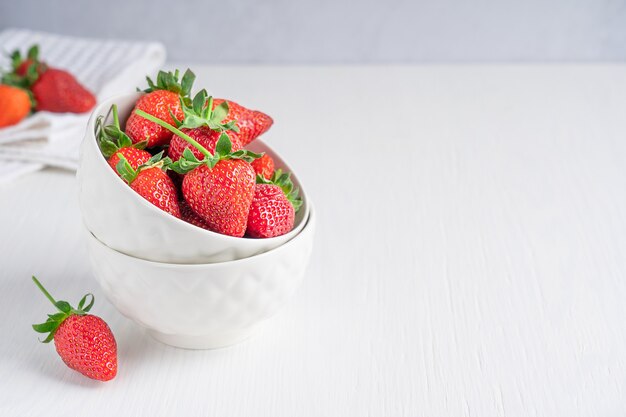 Fresh organic garden strawberries with juicy texture and sweetness in bowls on white wooden table