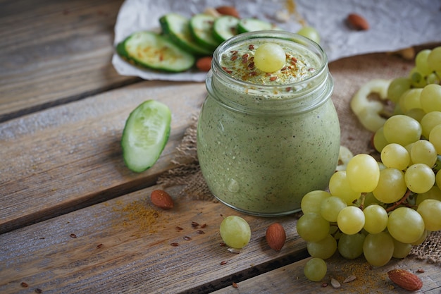 Frullato verde biologico fresco con cetriolo, prezzemolo, uva e sedano su fondo di legno rustico