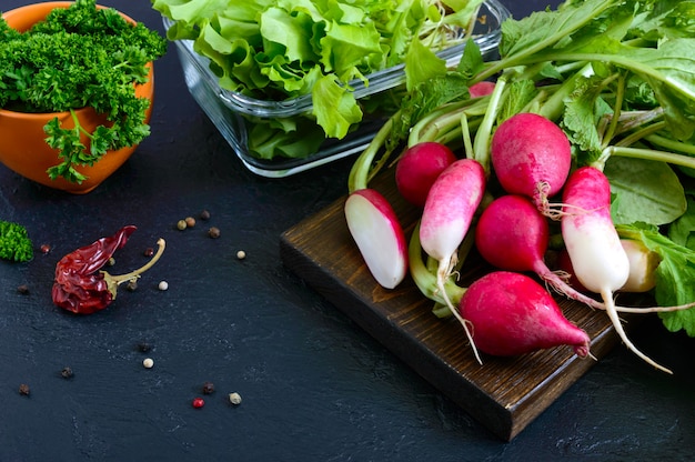 Photo fresh organic greens. radishes, curly parsley, young lettuce on a black background.