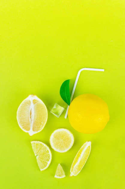 Fresh organic ice tea in abctract cup glass with yellow lemon lime fruit slice and green leaves, ice cube, straw on light green background. summer refreshing drink