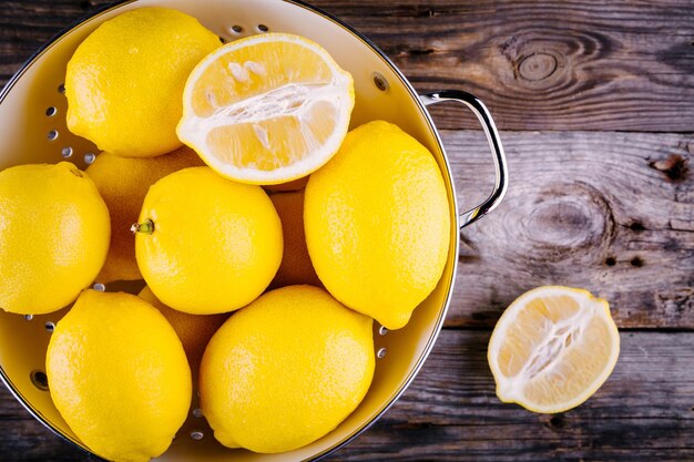 Fresh organic lemons in a colander on a wooden background view from above