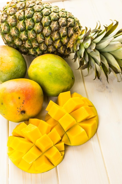 Fresh organic mango and pineapple on a white wood board.