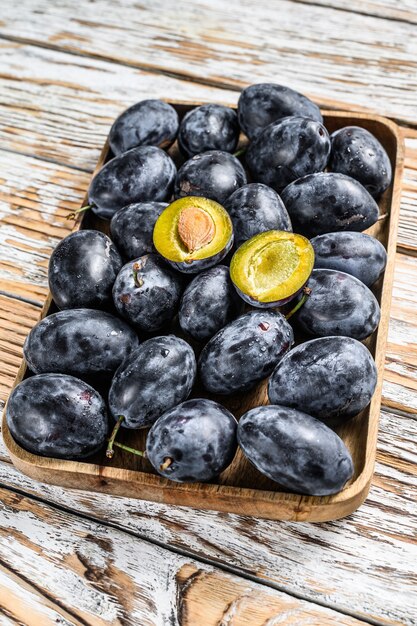 Fresh organic plums on a tray. White wooden background. Top view.