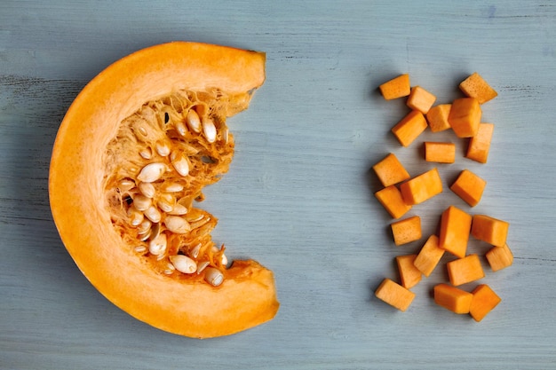 Fresh organic pumpkin slice and diced on a light blue wooden table.