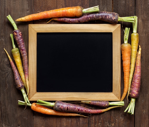 Fresh organic rainbow carrots and chalkboard on a wooden table top view