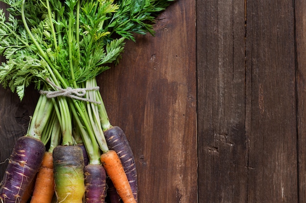 Fresh organic rainbow carrots with green tops on a wooden table top view