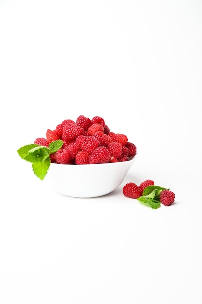 Fresh organic raspberries in a white bowl with a bit of mint isolated on white background with copy spaceVertical photo