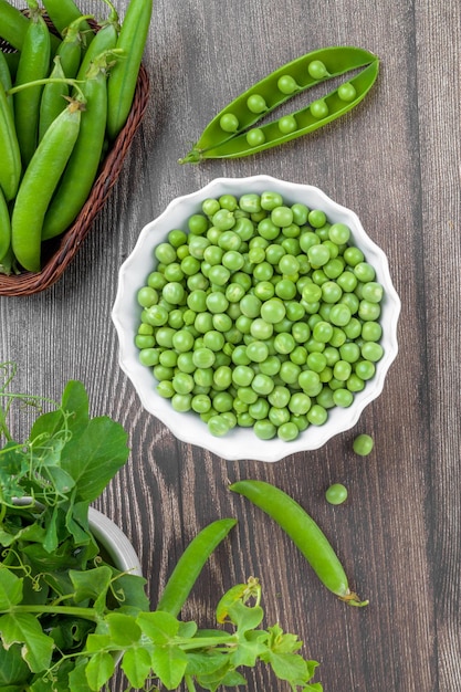Fresh organic raw green peas in a bowl with peas plants leaves on dark wooden table background bean protein close up
