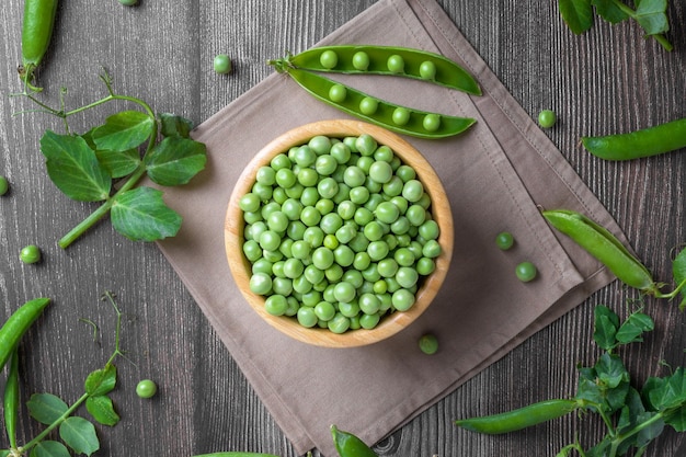 Fresh organic raw green peas in a bowl with peas plants leaves on dark wooden table background bean