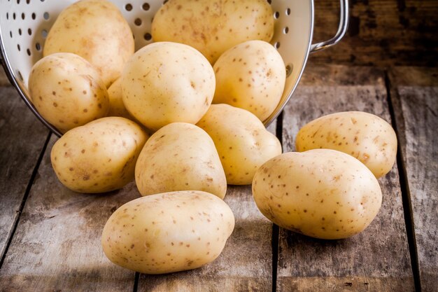 Patate crude organiche fresche in uno scolapasta su un tavolo rustico in legno