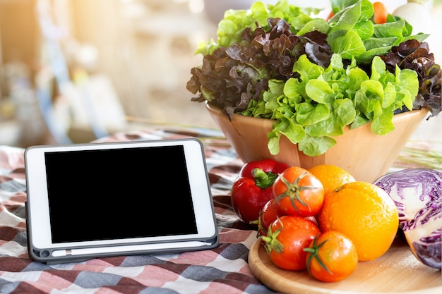 Fresh organic raw vegetable and fruit in bowl for salad and tablet on table