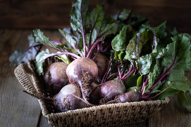 Fresh organic red beets with leaves in a wicker basket on a wooden table. Natural organic vegetables. Autumn harvest. Rustic