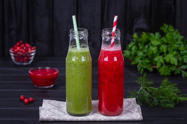 黒の木製テーブルの上のガラス瓶に新鮮な有機赤と緑の2つのスムージー、クローズアップ。さわやかな夏のフルーツドリンク。健康的な食事の概念。クランベリーとラズベリーのスムージー