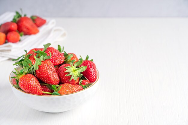 Fresh organic red sweet strawberries with juicy texture served in bowl on white wooden background