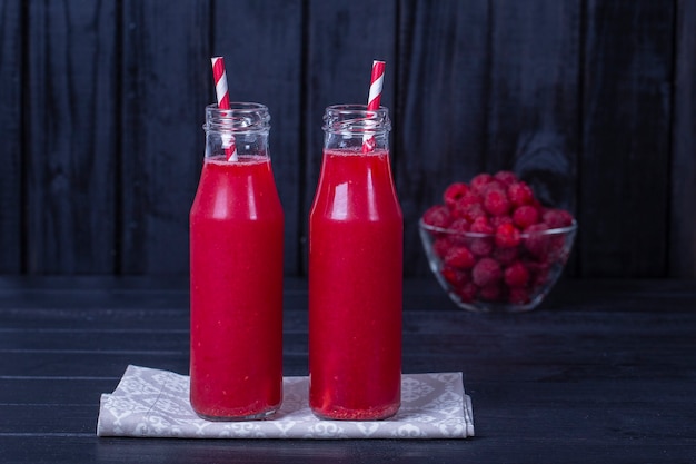 Fresh organic red two smoothie in glass bottle on black wooden table, close up. Refreshing summer fruit drink. The concept of healthy eating. Cranberry and raspberry smoothie