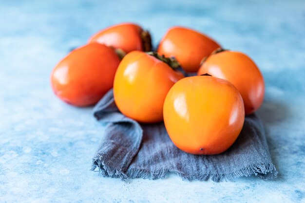 Fresh organic ripe persimmons on blue concrete background. Selective focus.