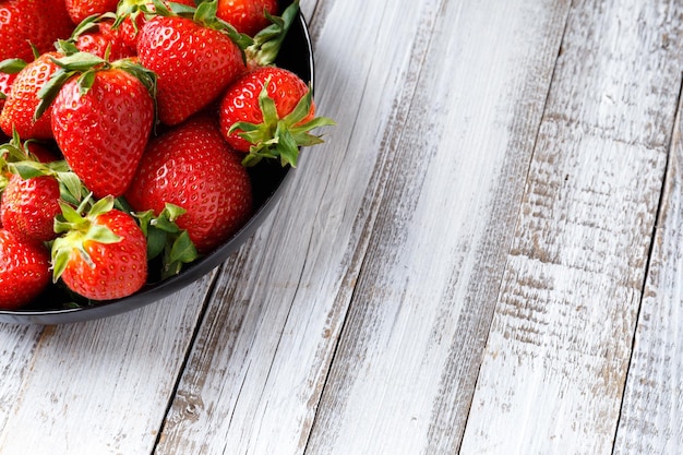 Fresh organic strawberries in a black round plate on a light wooden background with space for text