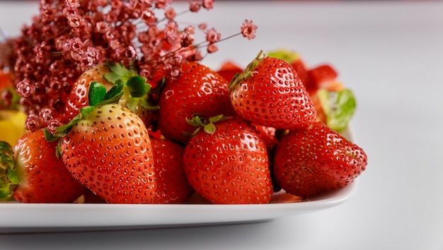 Fresh organic strawberries with flowers on plate on white background.