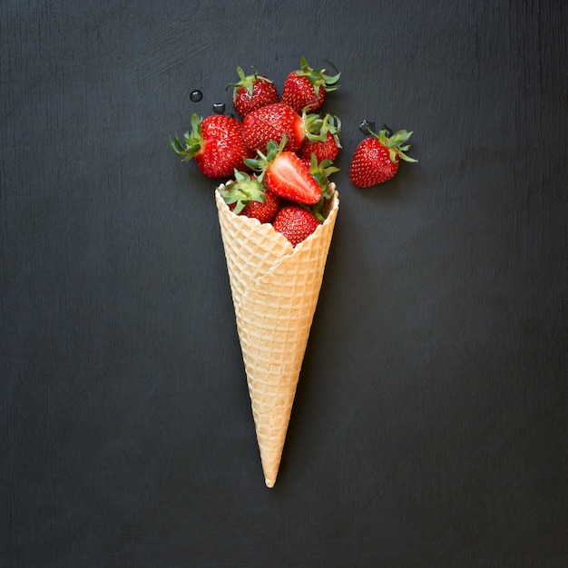 Fresh organic strawberry in ice cream cone on black.