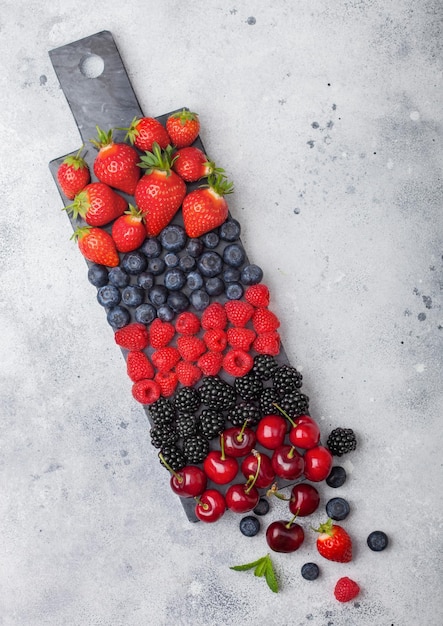 Mix di frutti di bosco estivi biologici freschi su tavola di marmo nero su sfondo tavolo da cucina chiaro lamponi fragole mirtilli more e ciliegie vista dall'alto