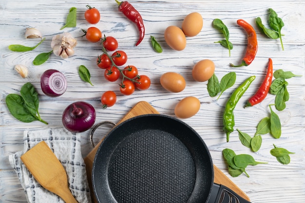 Pomodori, uova, cipolle, spinaci e pepe organici freschi sulla tavola di legno con la padella