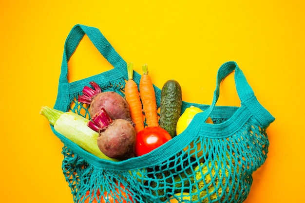 Fresh organic vegetables in cotton bag, lay on the yellow background. Conscious consumption