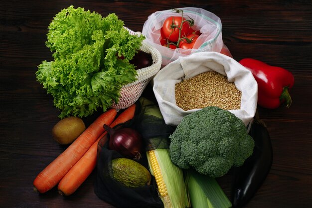 Свежие органические овощи в эко-мешках на деревянном столе. Безотходная концепция покупок и хранения продуктов