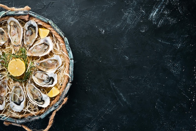 Fresh oysters with lemon in Wooden Box On a black stone background Top view Free copy space