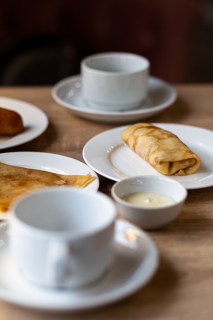 朝食用のコーヒーまたは紅茶用の白いマグカップの横にあるテーブルに詰め物が入った新鮮なパンケーキ。居心地の良いコーヒーで昼食後の甘いデザートのパンケーキ。