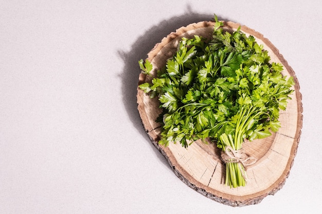 Fresh parsley as a cooking concept. Green herb bunch, wooden stand. A modern hard light, dark shadow, stone concrete background, top view