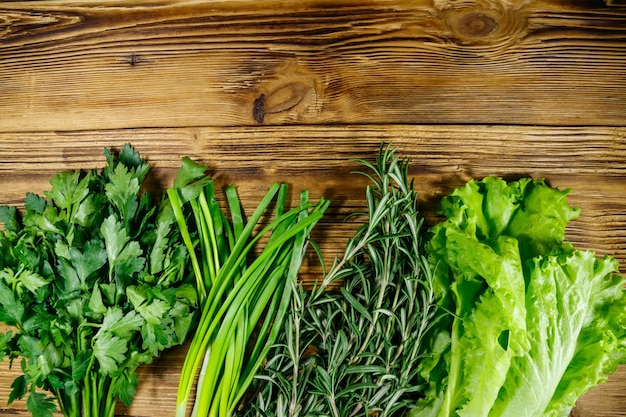 Fresh parsley lettuce leaves green onion and rosemary herbs on wooden table Top view