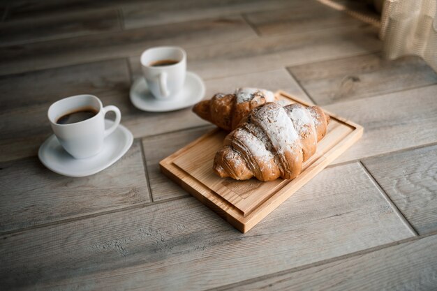 Fresh pastries croissants with chocolate on a wooden board and two cups of black coffee. Romantic breakfast