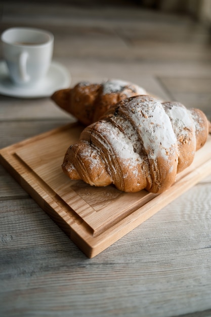 Fresh pastries croissants with chocolate on a wooden board and two cups of black coffee. Romantic breakfast