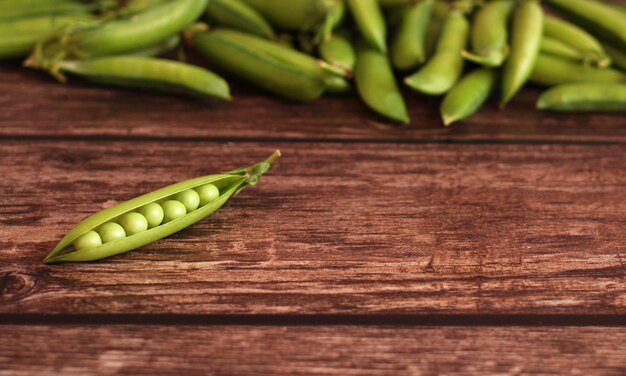 木製の背景にエンドウ豆で開いた新鮮なエンドウ豆の鞘