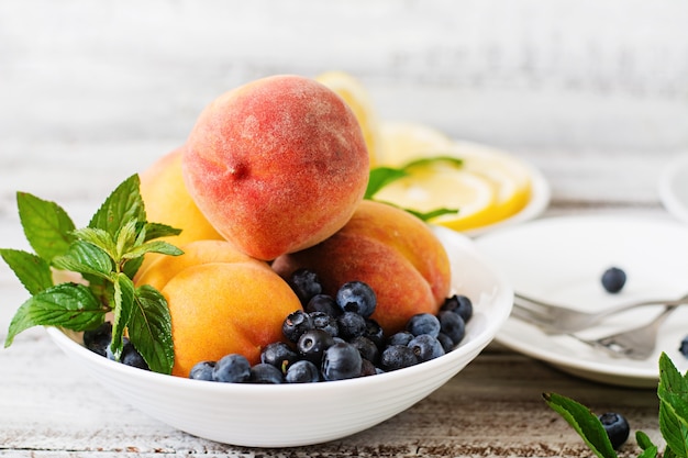 Fresh peaches and blueberries in bowl on a light wooden background in rustic style