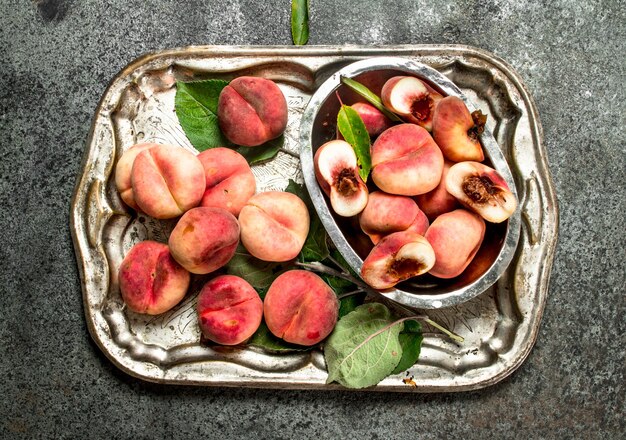 Fresh peaches in a bowl on a steel tray. On a rustic background.