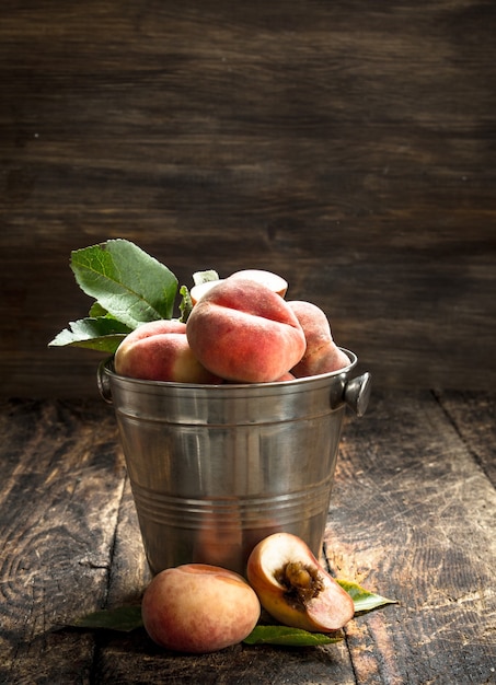 Fresh peaches in a bucket with leaves on a wooden background