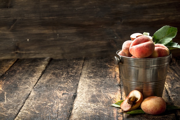 Fresh peaches in a bucket with leaves. On a wooden table.