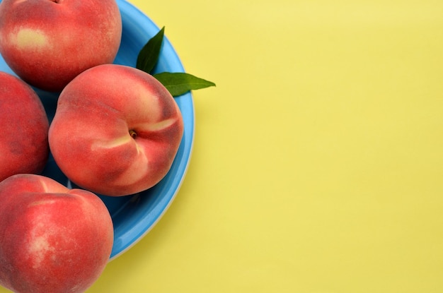 Fresh peaches on a plate on a light yellow background copy space