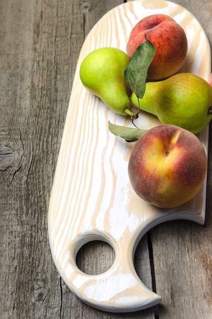 Fresh pears and peaches on wooden cutting board