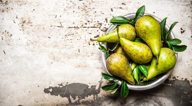 Fresh pears with leaves in the bowl. On rustic background. Free space for text . Top view