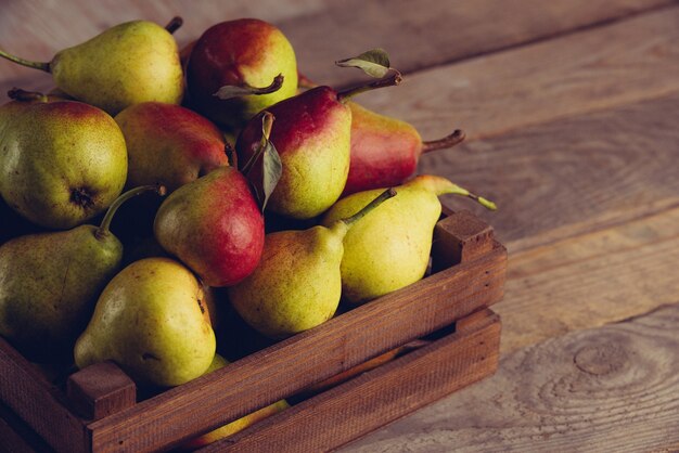 Pere fresche con foglie in una scatola di legno su sfondo di legno.