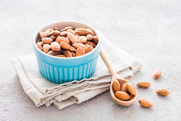 Fresh peeled almonds in a wooden spoon and in a bowl nearby on a light background. A source of vitamins and oils. Organic food. Copy space