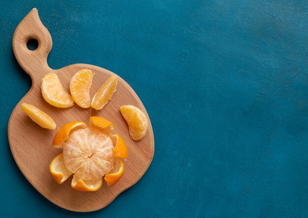 Fresh peeled mandarin on wooden board on blue with copy space